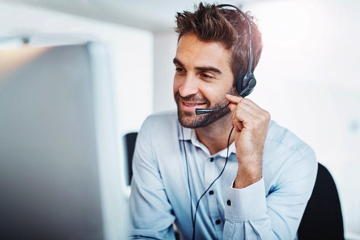 A man speaking into the microphone of a headset while sitting at a computer.