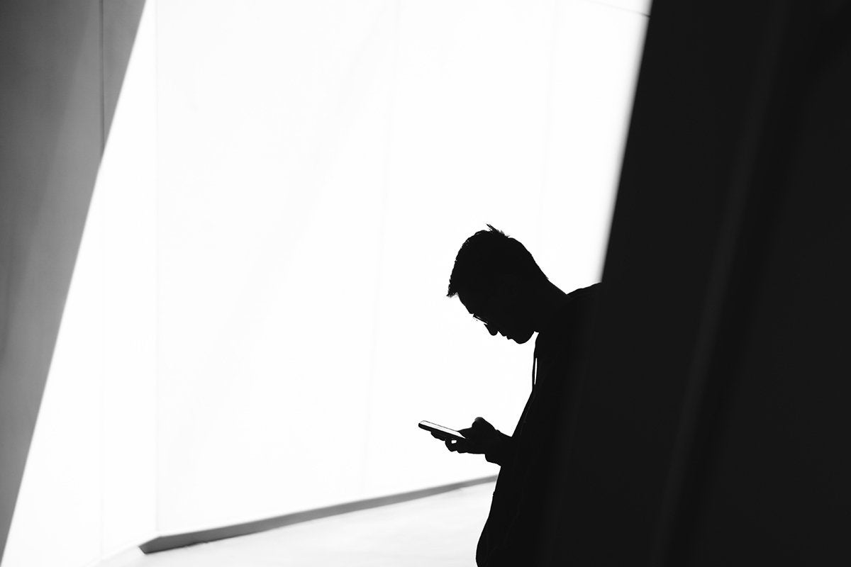 A man using a mobile phone in shadow against a bright wall
