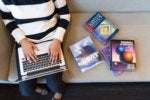 A woman using a laptop, surrounded by books on computing / programming / coding / development / Java