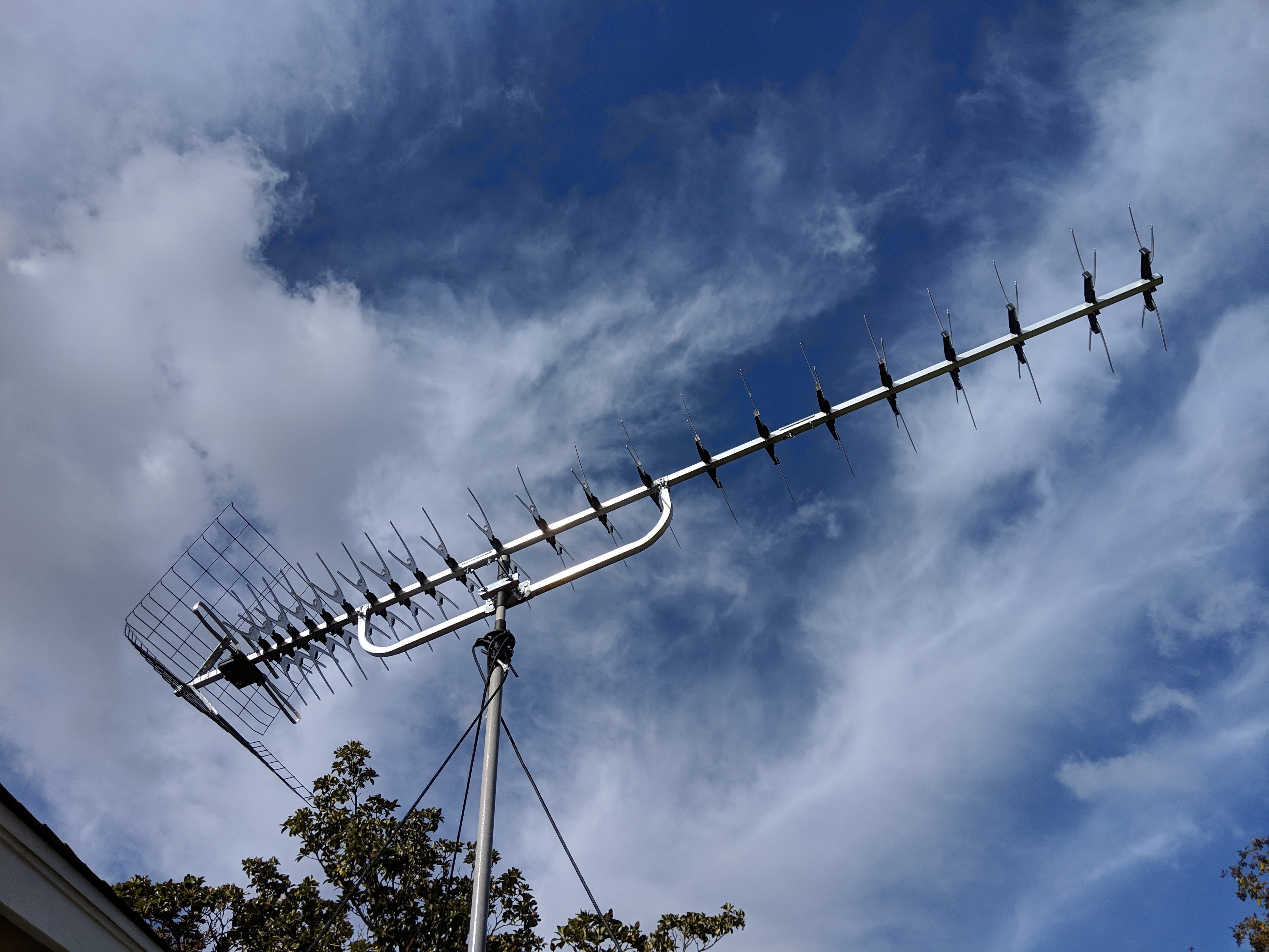  A roof-mounted TV antenna is shown with a blue sky and white clouds in the background.