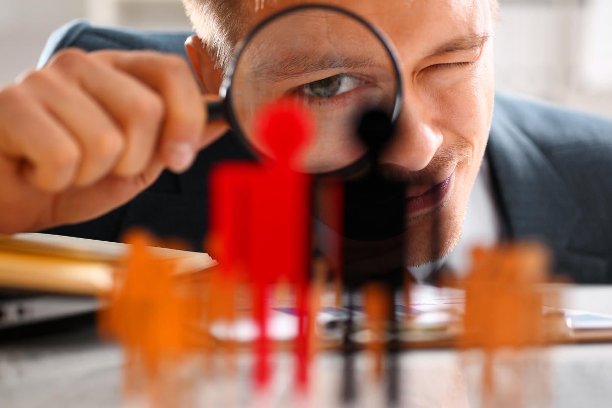 A man looks through a magnifying lens at a group of figurines.