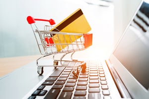 A miniature shopping cart with a credit card sits on computer keyboard.