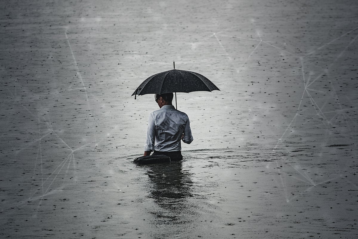A man with an umbrella stands waist-deep in water as rain continues to fall.
