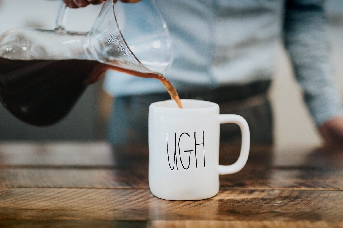 A man pours coffee into a mug that reads 'UGH.'
