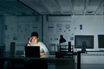A stressed employee works alone in a dimly lit office.