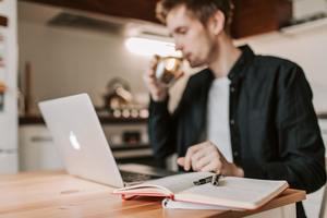 crop male freelancer drinking water while watching laptop in 4050445