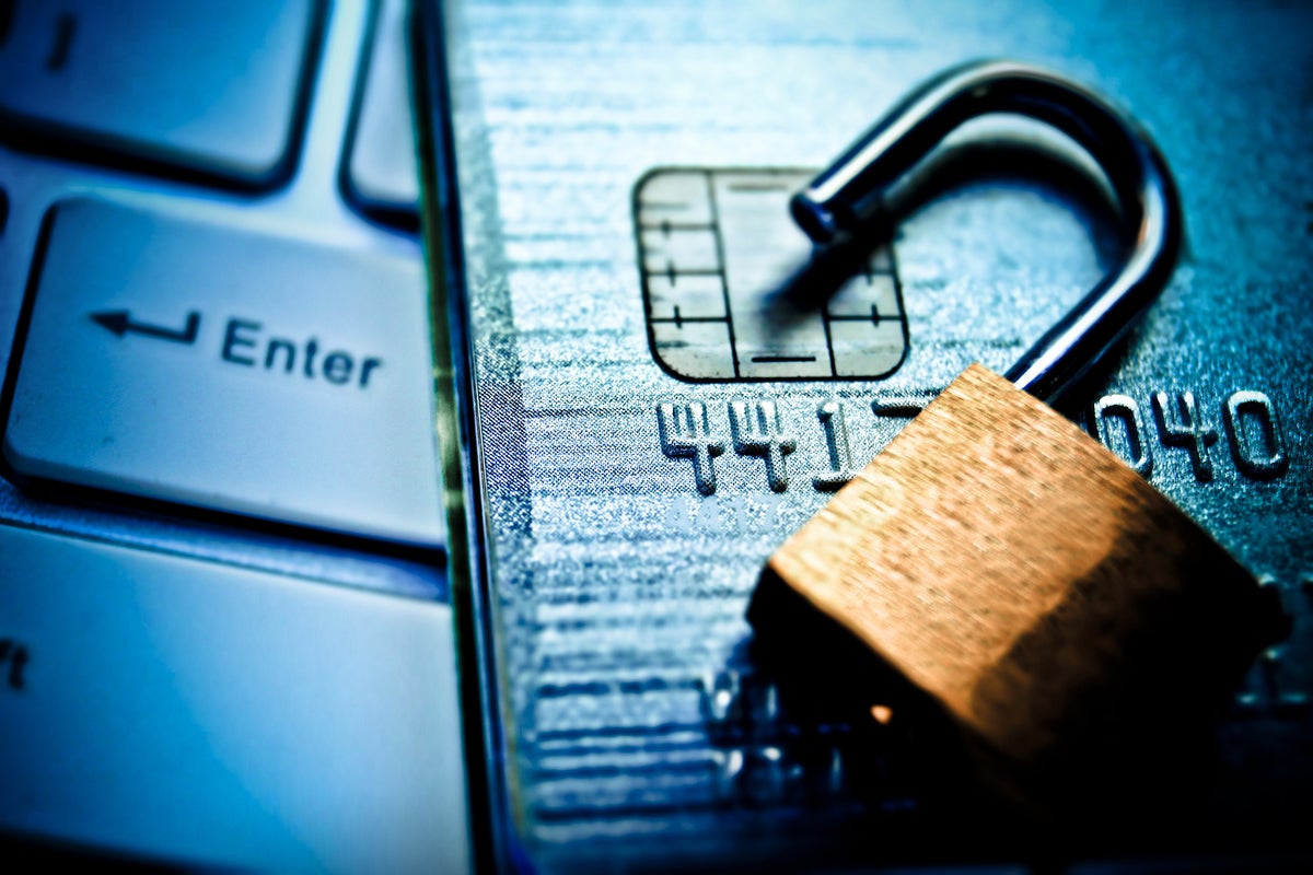 An open lock sits on a credit card lying on a computer keyboard.