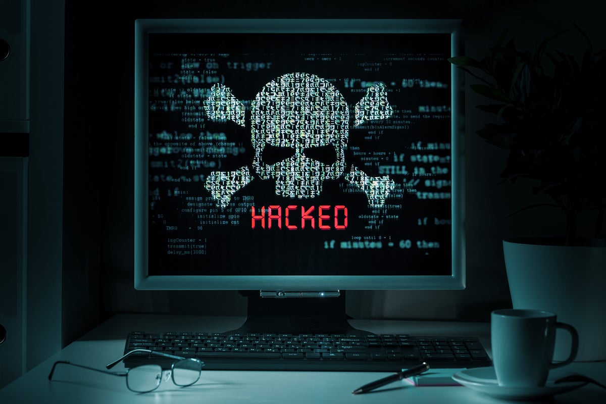 A computer monitor displays abstract data, a skill and crossbones, and 'HACKED.'