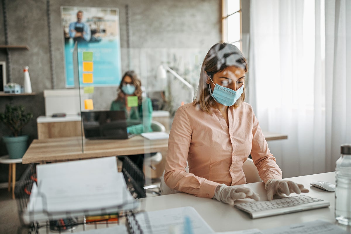 Co-workers use protective face masks and glass partitions in a post-COVID workspace.