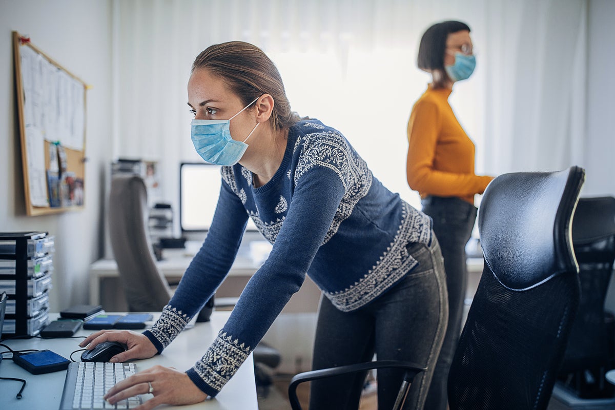 Co-workers wear protective face masks in a post-COVID office workspace.
