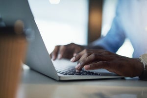 Hands type on a laptop keyboard.
