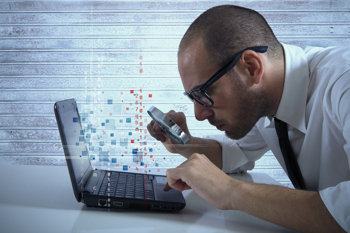 A laptop user with magnifying lens examines binary data.