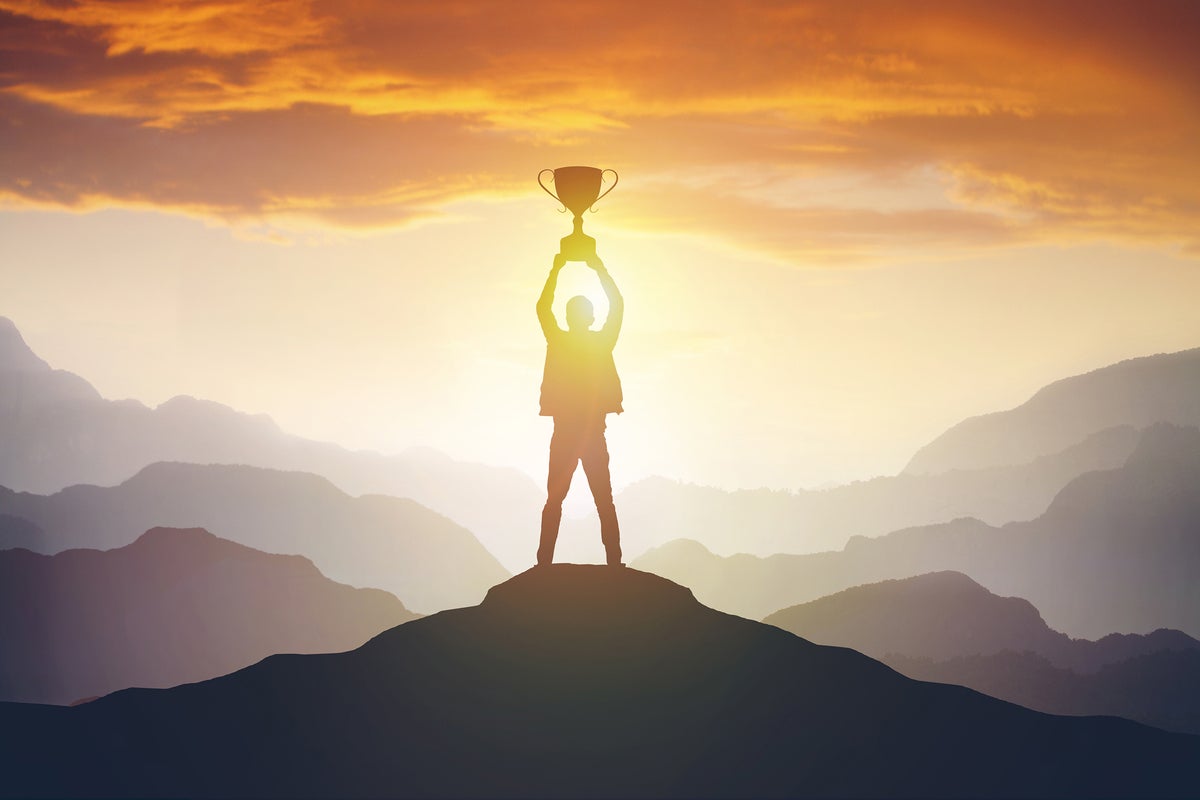 On a mountaintop, a man holds a trophy at sunset. [success / achievement / recognition]