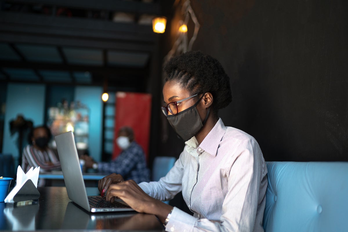 A woman wears a protective face mask while using a laptop in a shared space.