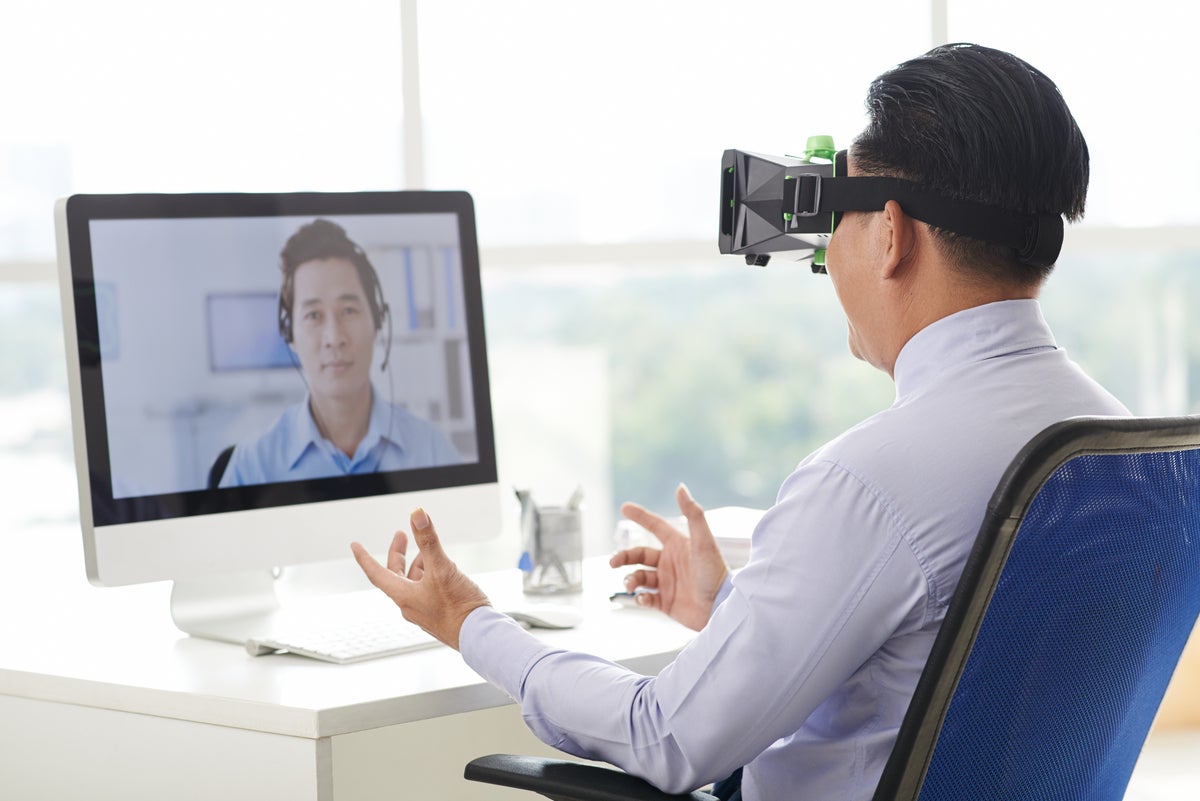 Businessman in virtual reality goggles having video call with coworker