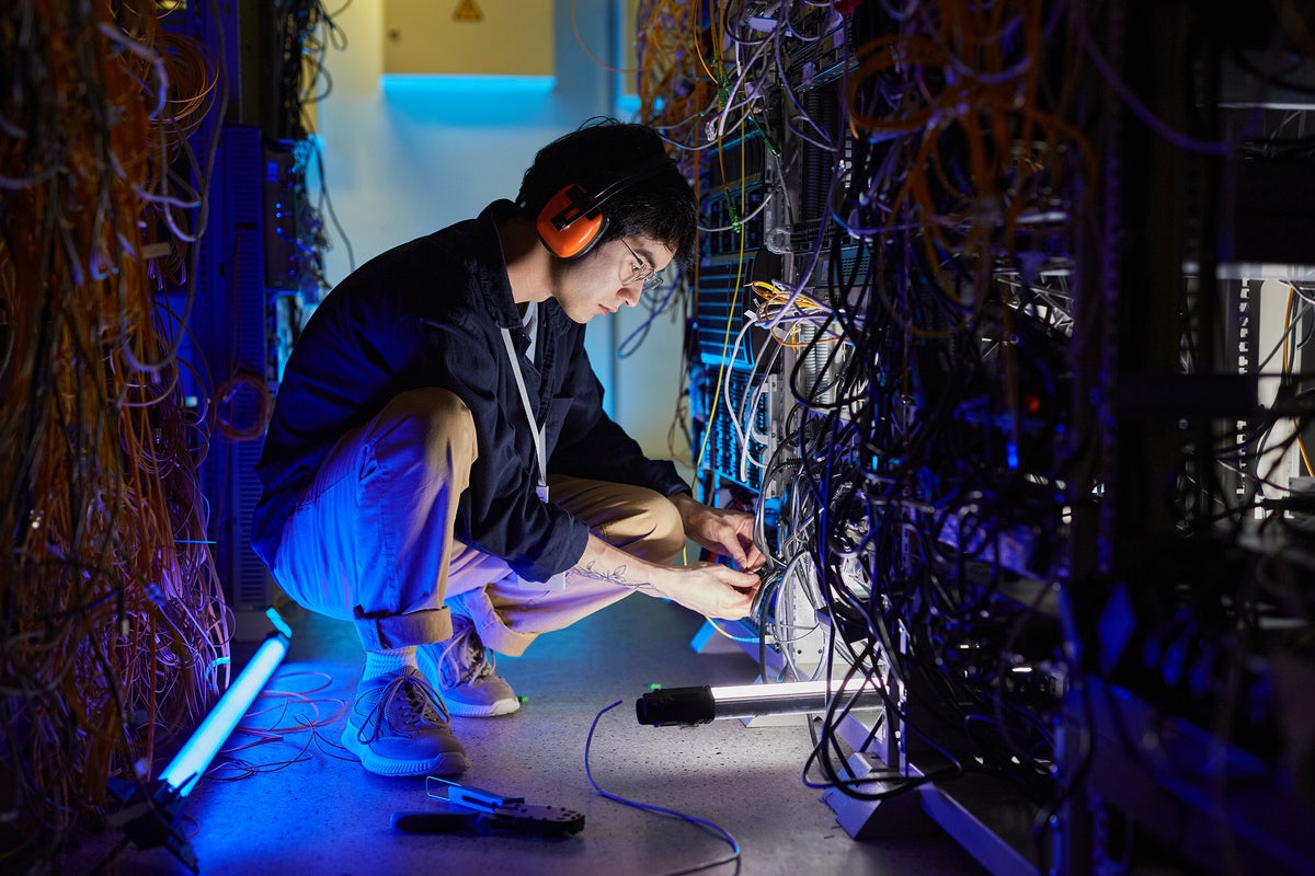 A developer / engineer / technician works with servers, wires, and cables in a data center.