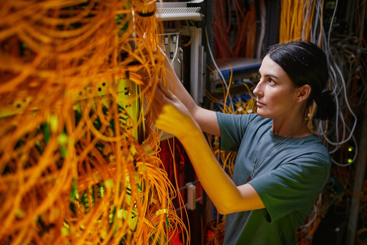 A developer / engineer / technician works with servers, wires, and cables in a data center.