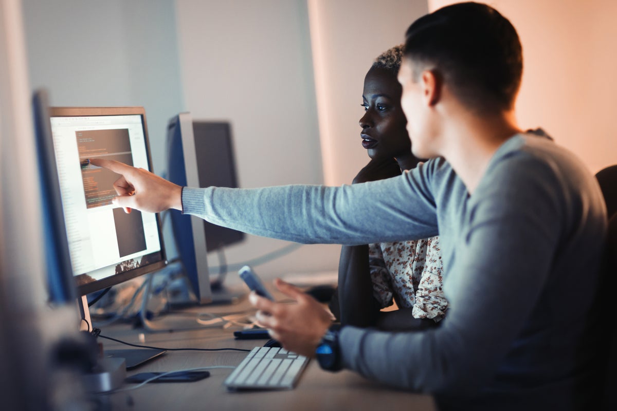 Developers work together to review lines of code in an office workspace.