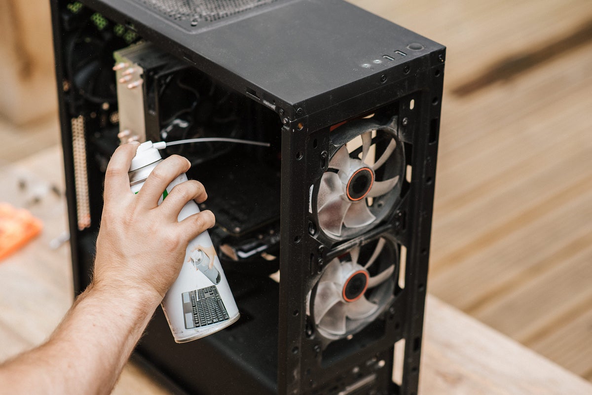 person uses can of compressed air to clean out PC