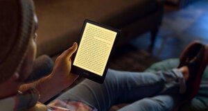 person with a hat holding a 5th generation Kindle Paperwhite