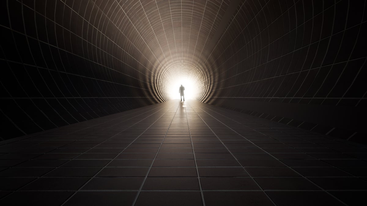 shutterstock 1901776579 figure walking toward bright light at the end of a dark tunnel