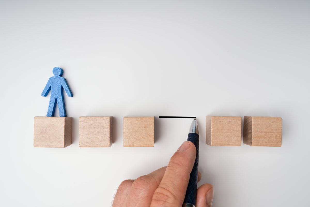 Human Hand Filling Gap Between Wooden Blocks Arranged In A Row With Blue Human Figure