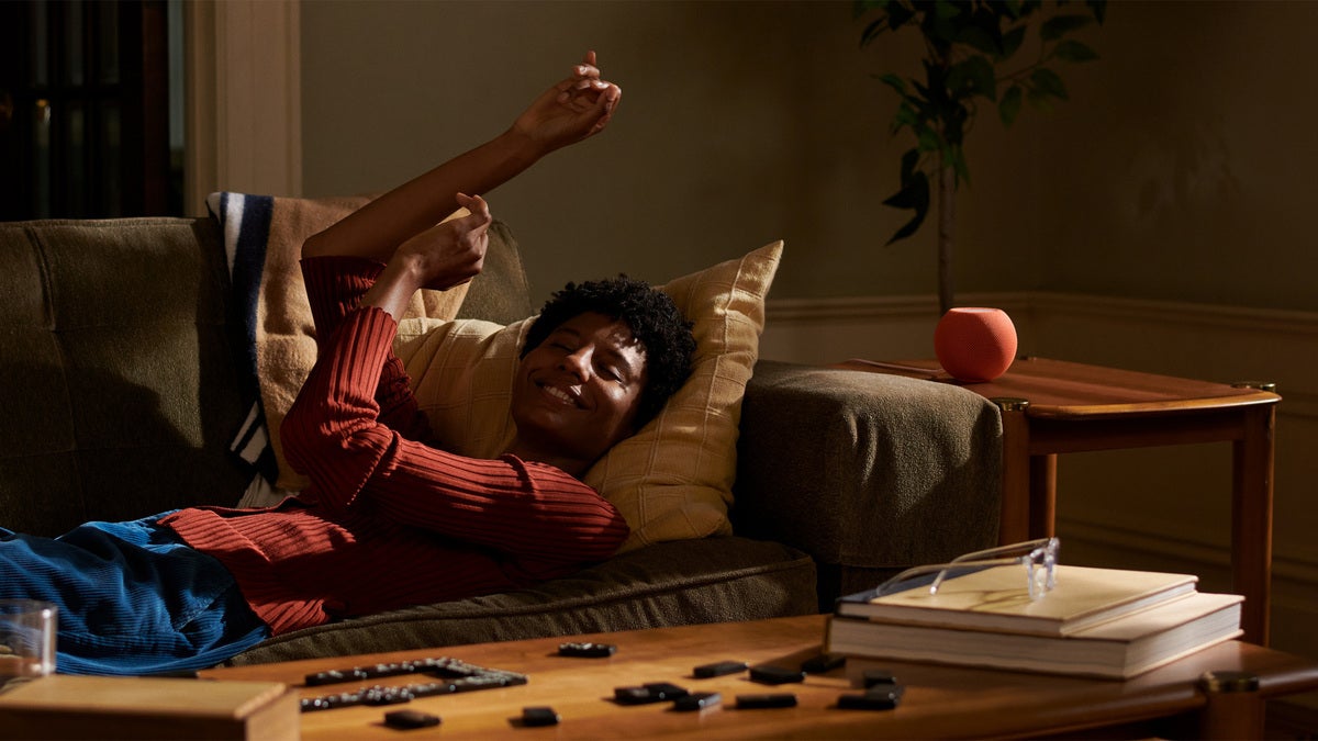 Mujer estirada en el sofá con un HomePod mini naranja